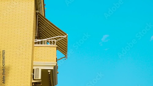 Striped retractable awning on apartment balcony under bright blue sky. Residential building facade with outdoor sunshade and air conditioner. Mediterranean urban lifestyle in Spain
