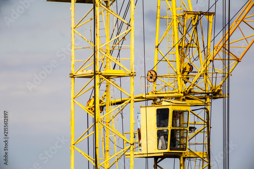 Foto Close-up of a yellow construction crane operator cabin and lattice boom structure against a grey sky, indicating ongoing building work at a site for panel house construction