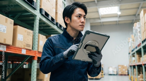 物流倉庫でタブレット端末を操作しながら棚の在庫を確認する日本人男性の倉庫作業員