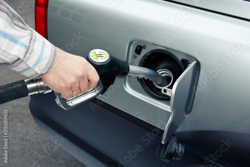 Hand holding fuel nozzle to refuel car with green energy