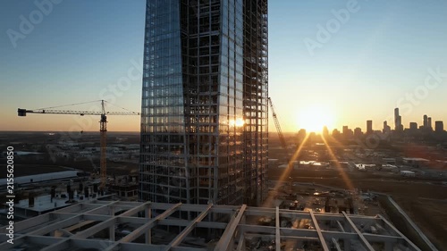 Construction site at sunset, steel beams of skyscraper frame against the sky, urban skyline in background