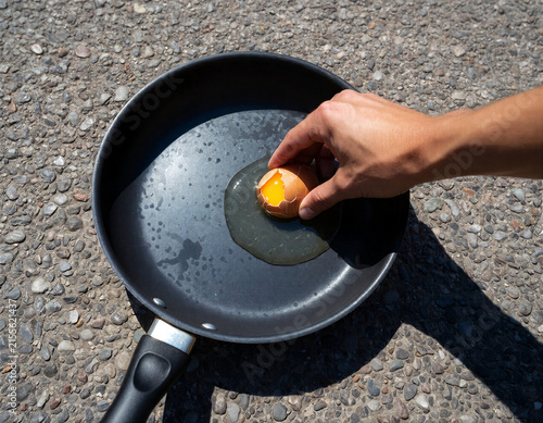 Hand cracking raw egg into frying pan on hot asphalt in a very hot day, during a heatwave