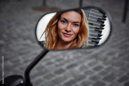 Portrait of smiling young woman reflected in wing mirror of a motorcycle
