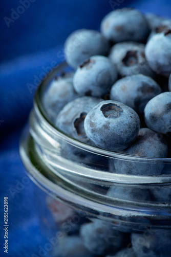 Glass jar with blueberries on blue textured fabric. Dark background.
