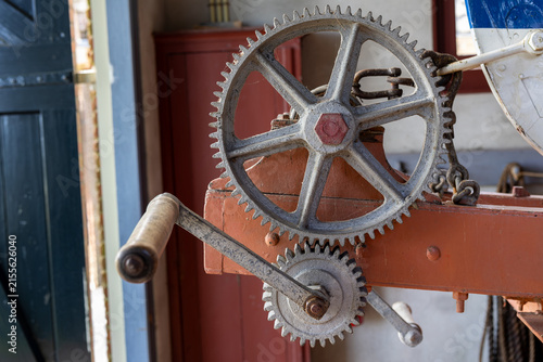 Canvastavla Close-up of an old boat trailer gear mechanism with metal cogwheels, a hand crank and worn painted parts, showing vintage mechanical detail in a historic maritime setting