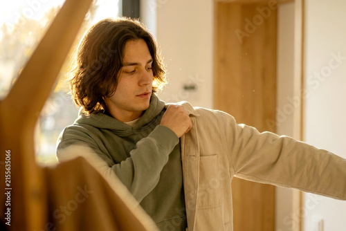 Young man putting on jacket at home in golden morning light