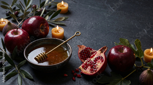 Rosh Hashanah Celebration Concept Traditional Jewish Holiday Foods Pomegranate Red Apples Honey Dipper Bowl Olive Branches Wax Candles Dark Stone Background Still Life Autumn Harvest Festive Table