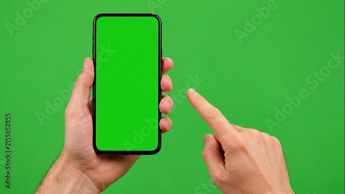 Person pointing at smartphone with green screen in studio