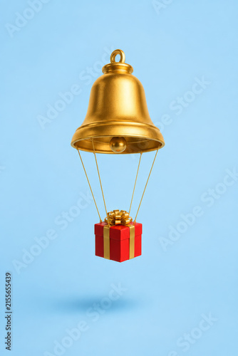 A single elegant golden Christmas bell transformed into a miniature hot air balloon, a tiny wrapped Christmas gift functioning as the basket beneath. Minimalist conceptual Christmas background