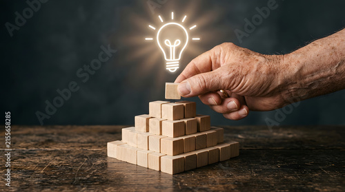Hand placing a wooden block on top of a pyramid with a glowing light bulb icon
