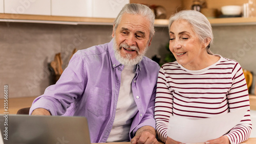 фотографія Smiling Elderly Couple, Man And Woman, Engaged And Enjoying Time Together Using Laptop In Cozy Home Setting, Sharing Joyful Moments