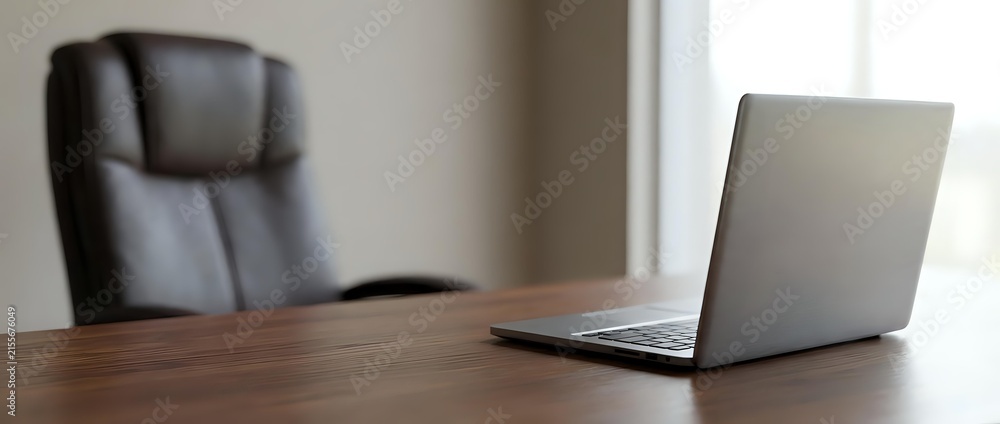 Fototapeta premium Laptop on wooden desk with empty office chair in background