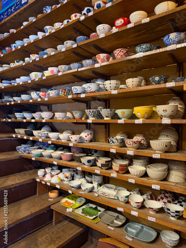 Traditional Japanese ceramic bowls and tableware displayed on wooden shelves in a pottery shop in Kappabashi, Tokyo, showcasing colorful patterns, handmade designs and Japanese craftsmanship