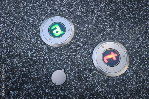 Circular symbols embedded into the ground represent adenine (a) and thymine (t), two of the four primary chemical bases that form DNA, Pedestrian direction lights embedded in the walkway