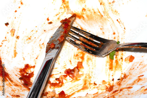 Close up of a messy dirty used white plate with cutlery on