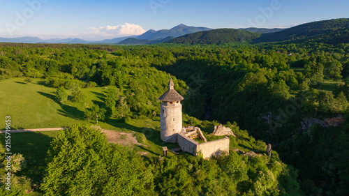 Drone shot displays rural landscape of Dreznik old tower near Plitvice Lakes. Green fields, farm lands, and countryside roads spread across traditional Croatian village territory.