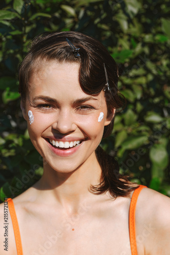 Fotografie Smiling woman with natural skin texture applying white cream on her face outdoors, celebrating authentic beauty, real skin, and selfcare