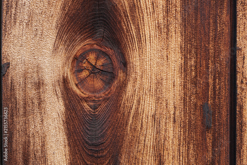 Close-up of a circular knot resembling a human eye on the left side of a lightly charred wooden surface with swirling grain lines.