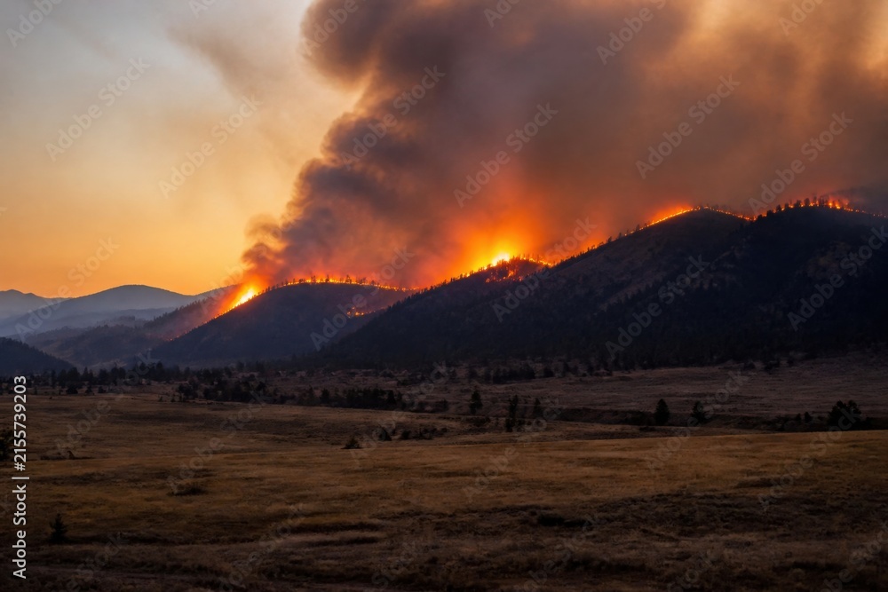 Fototapeta premium Distant wildfire burning across a dry forest ridge beneath a massive smoke column for wildfire preparedness, property protection and climate campaigns