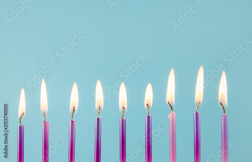 9 metallic pink and purple color birthday candles burning in a row isolated on blue background. Happy Birthday card design concept.  Bottom lower border edge a lot of copy space.