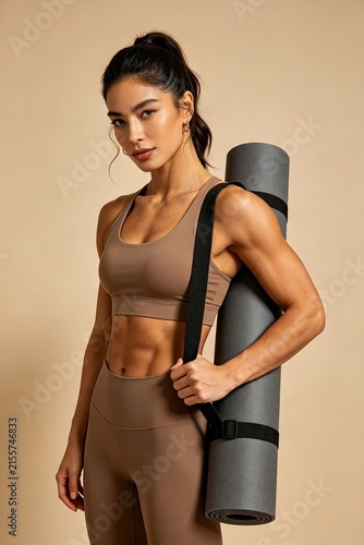 Athletic woman standing with a yoga mat in sportswear, healthy active lifestyle, fitness training, wellness, strength and exercise concept