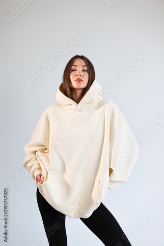 Young woman presenting empty cream hooded sweatshirt mockup, casual streetwear.
