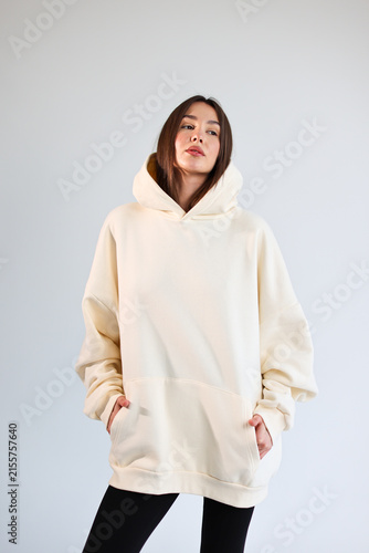 Young woman presenting empty cream hooded sweatshirt mockup, casual streetwear.