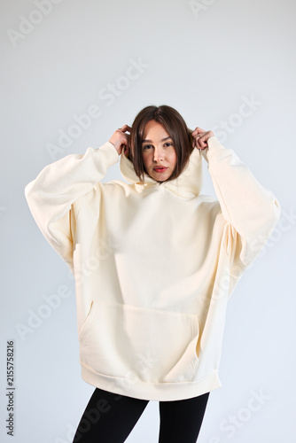 Young woman presenting empty cream hooded sweatshirt mockup, casual streetwear.