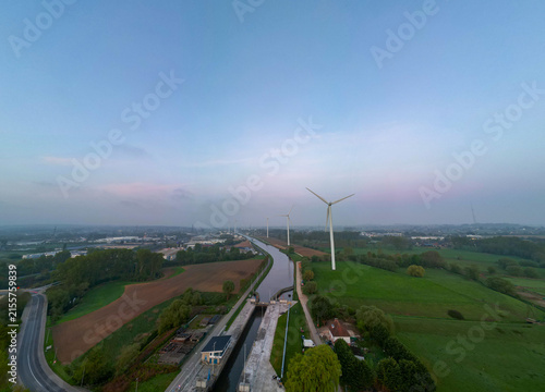 Lot, Beersel, Vlaams-Brabant, 22nd of April, 2025, A breathtaking aerial shot showcasing numerous wind turbines, a winding road, and lush, vibrant greenery