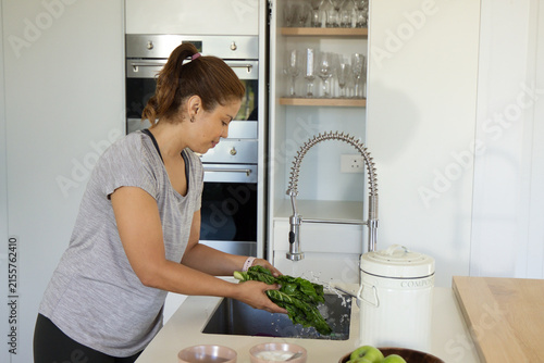 Bild auf Leinwand African American adult woman washing leafy greens under spring-coil faucet at mo