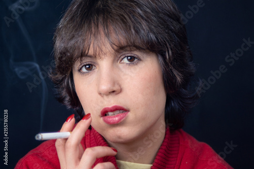 Portrait of young female smoker in red sweater, smoking cigarette, dark backdrop