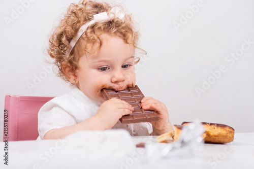 Young girl bites into chocolate bar while seated at table