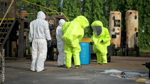 Hazmat workers in protective suits handle a chemical container during hazardous material response training at an industrial facility