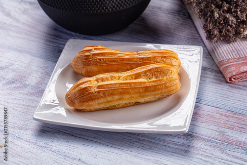 Bild auf Leinwand Two golden eclairs on white plate with rustic wooden background
