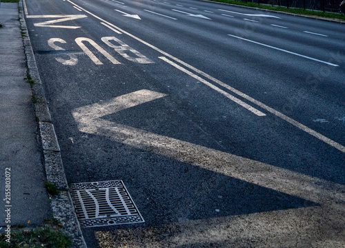 White road marking paint and symbols painted on dark asphalt street surface outdoors bus station