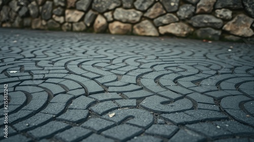 A  patterned  pavement  composed  of  interlocking  stone  segments  with  a  stone  wall  blurred  in  the  background