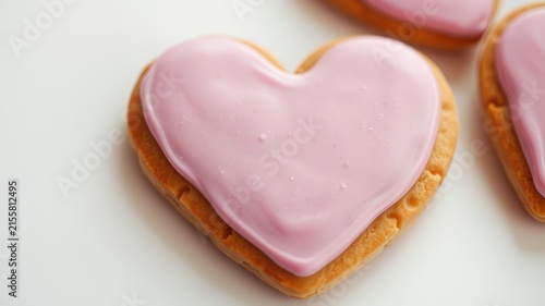 A heart-shaped cookie, frosted in a delicate shade of pink, sits on a plain white background, inviting a sweet and simple treat.