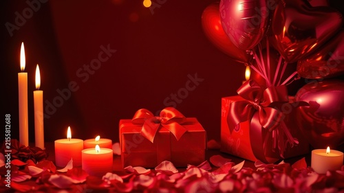 Red gift box with a bow surrounded by candles, rose petals, and heart shaped balloons on a red background