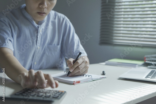 Close-up of hands using a calculator while pointing with a pen at numbers in an accounting notebook. Finance Home business