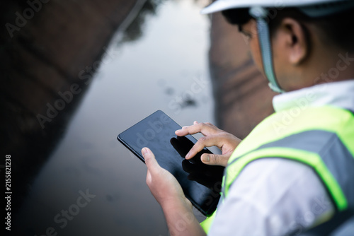 Environmental engineer testing water quality in irrigation canal using field equipment and tablet.