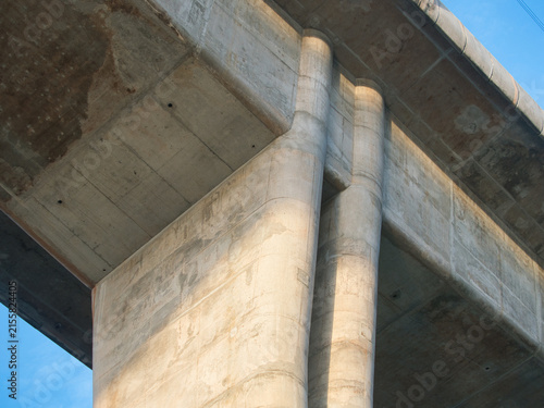 Low-angle view of a reinforced concrete bridge spanning a river an elevated highway structure set against a clear blue sky.