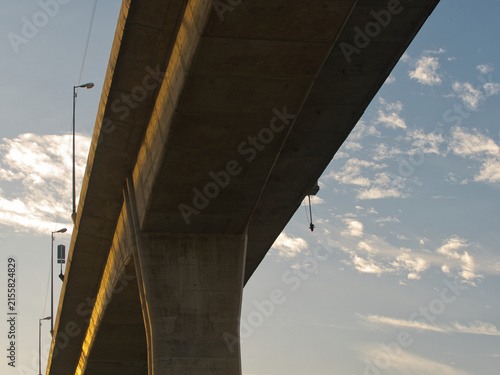 Low-angle view of a reinforced concrete bridge spanning a river an elevated highway structure set against a clear blue sky.