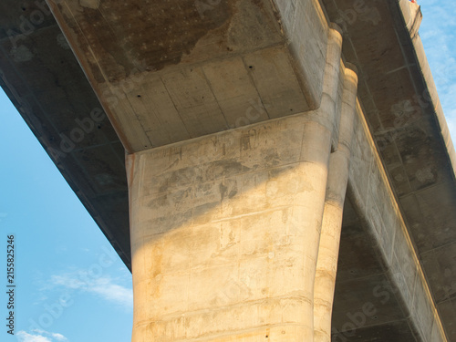 Low-angle view of a reinforced concrete bridge spanning a river an elevated highway structure set against a clear blue sky.