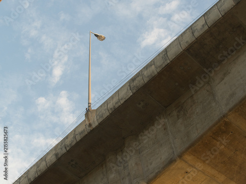 Low-angle view of a reinforced concrete bridge spanning a river an elevated highway structure set against a clear blue sky.