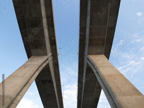 Low-angle view of a reinforced concrete bridge spanning a river an elevated highway structure set against a clear blue sky.