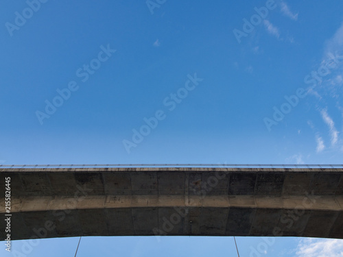Low-angle view of a reinforced concrete bridge spanning a river an elevated highway structure set against a clear blue sky.