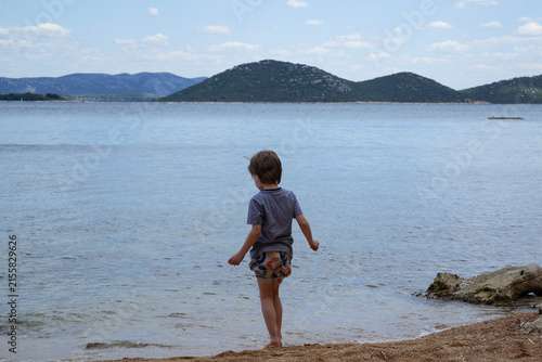 Little boy standing on the shore looking at the calm sea and islands in Vrgada, Croatia
