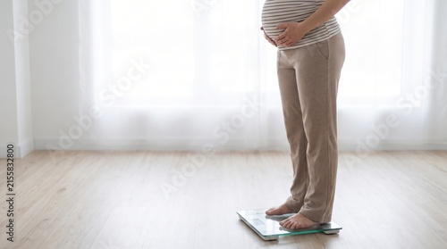 Pregnant woman standing on a digital scale in a bright room to monitor health during pregnancy