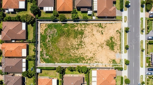 A sunny day aerial view showing an empty plot of land surrounded by residential houses