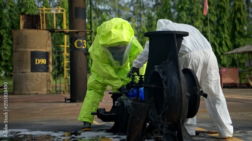 Hazmat workers in protective suits handle a chemical container during hazardous material response training at an industrial facility